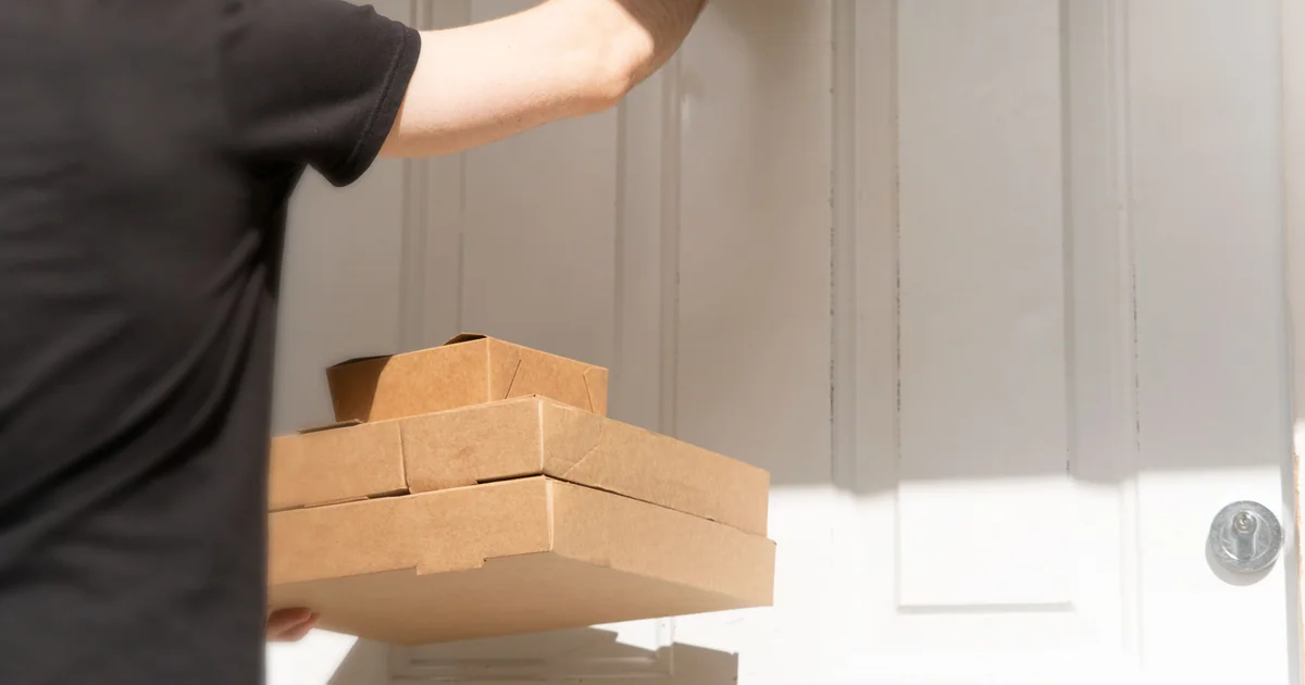 Entregador com caixas em frente à porta de um cliente durante uma entrega